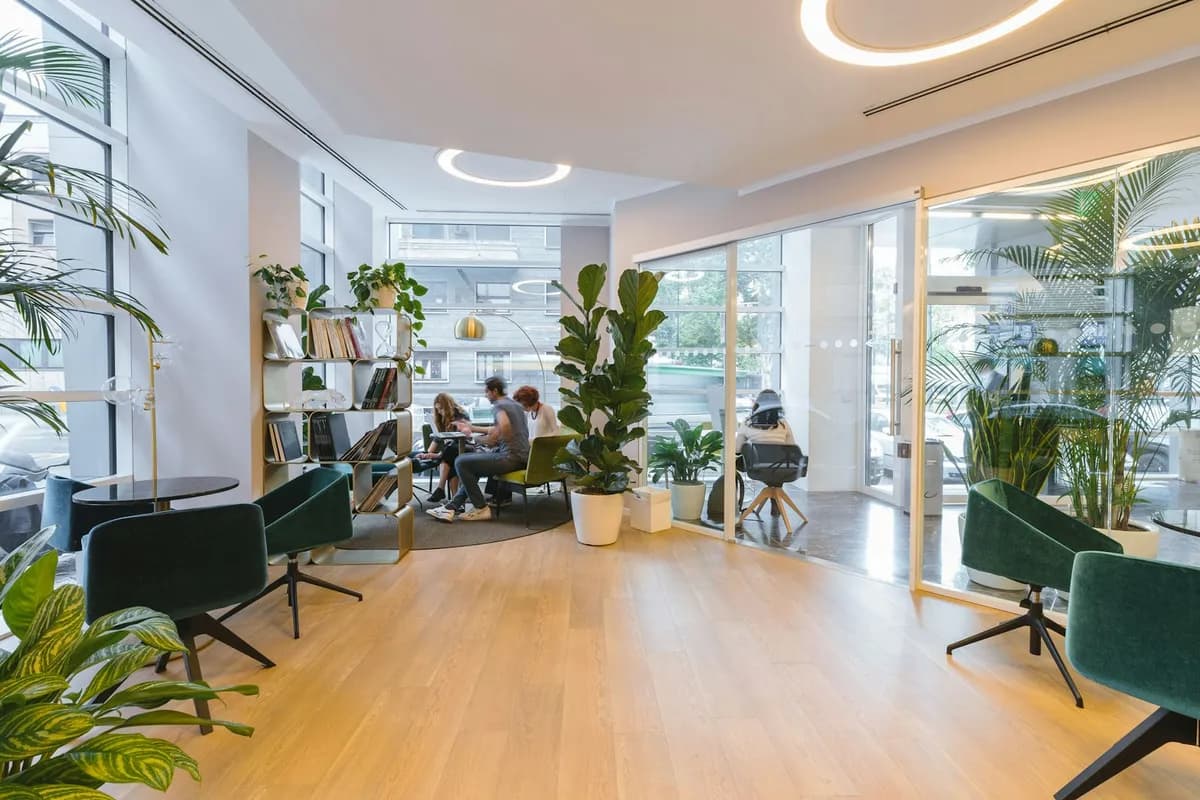 Svijetli coworking prostor sa zelenim foteljama, biljkama i ljudima koji rade za stolom